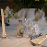 Une table élégamment dressée avec une bouteille artisanale de punch "Ti Tonton", mise en valeur au centre d’un décor floral raffiné.
