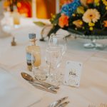 Une table élégamment dressée avec une bouteille artisanale de punch "Ti Tonton", mise en valeur au centre d’un décor floral raffiné.